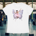 A white short-sleeve crewneck t-shirt featuring a graphic print of a ballerina with butterfly wings in a pink tutu, displayed against a blurred indoor stage background with a band and instruments.